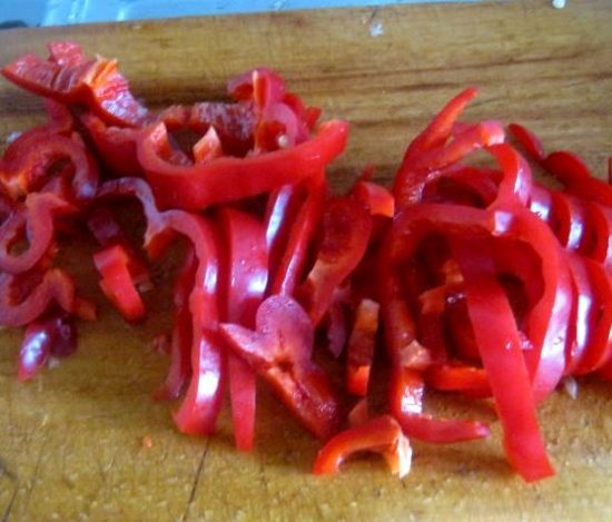 Нарезанный соломкой красный сладкий перец на деревянной разделочной доске